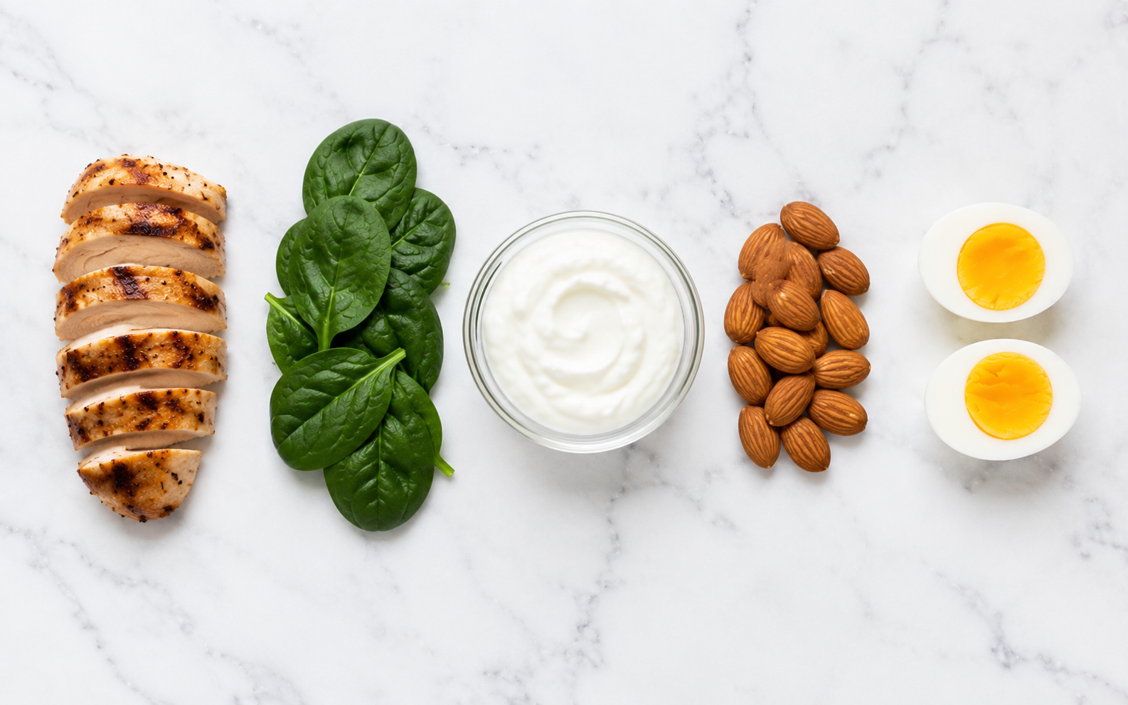 Five foods showing the nutrients most at risk when maintaining nutrition in a deficit — chicken (protein), spinach (iron), Greek yogurt (calcium), almonds (magnesium), eggs (B vitamins)
